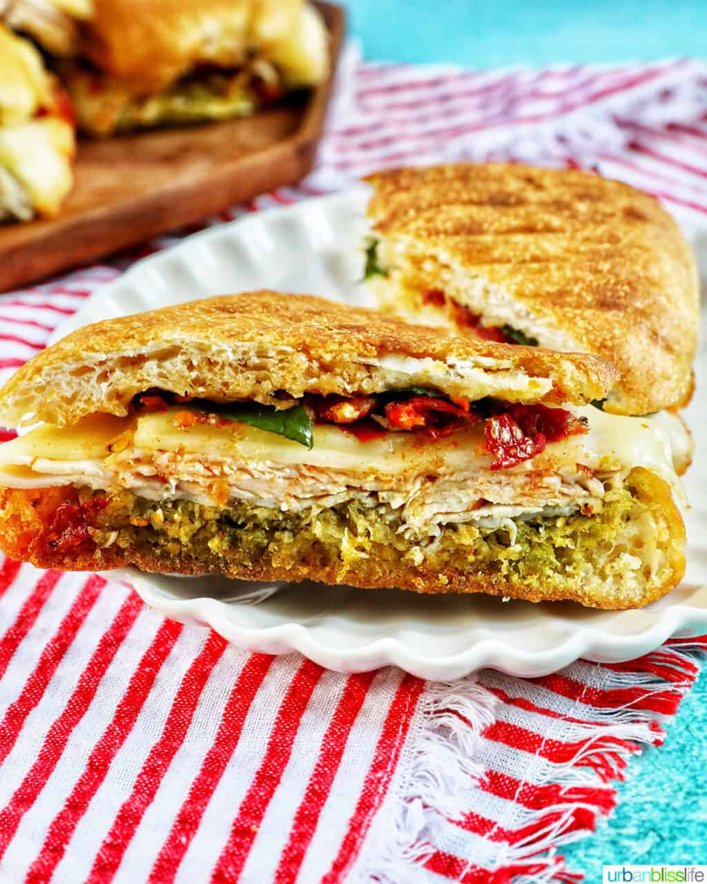 turkey pesto sandwich cut in half on a white plate with red striped napkin underneath.