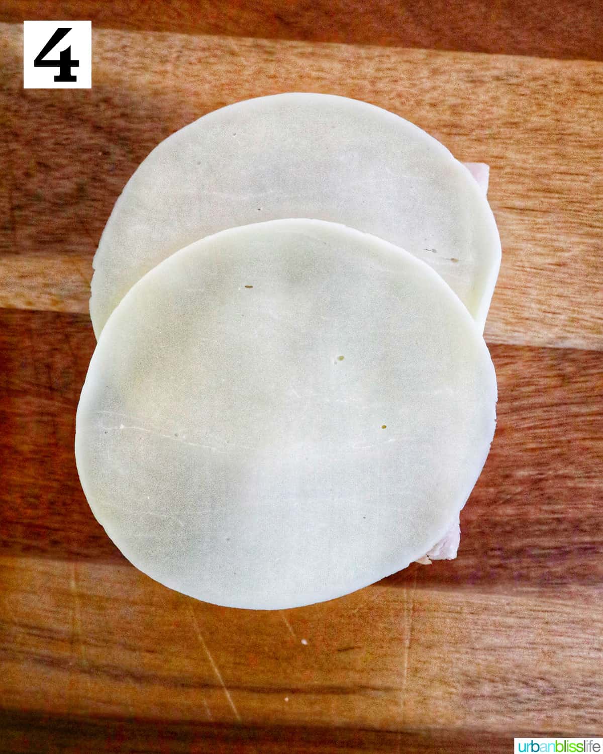 sliced round Provolone cheese on top of meat on a cutting board.