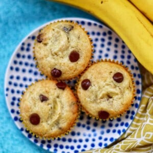 banana chocolate chip muffins on a polka dot plate with bananas on the side.