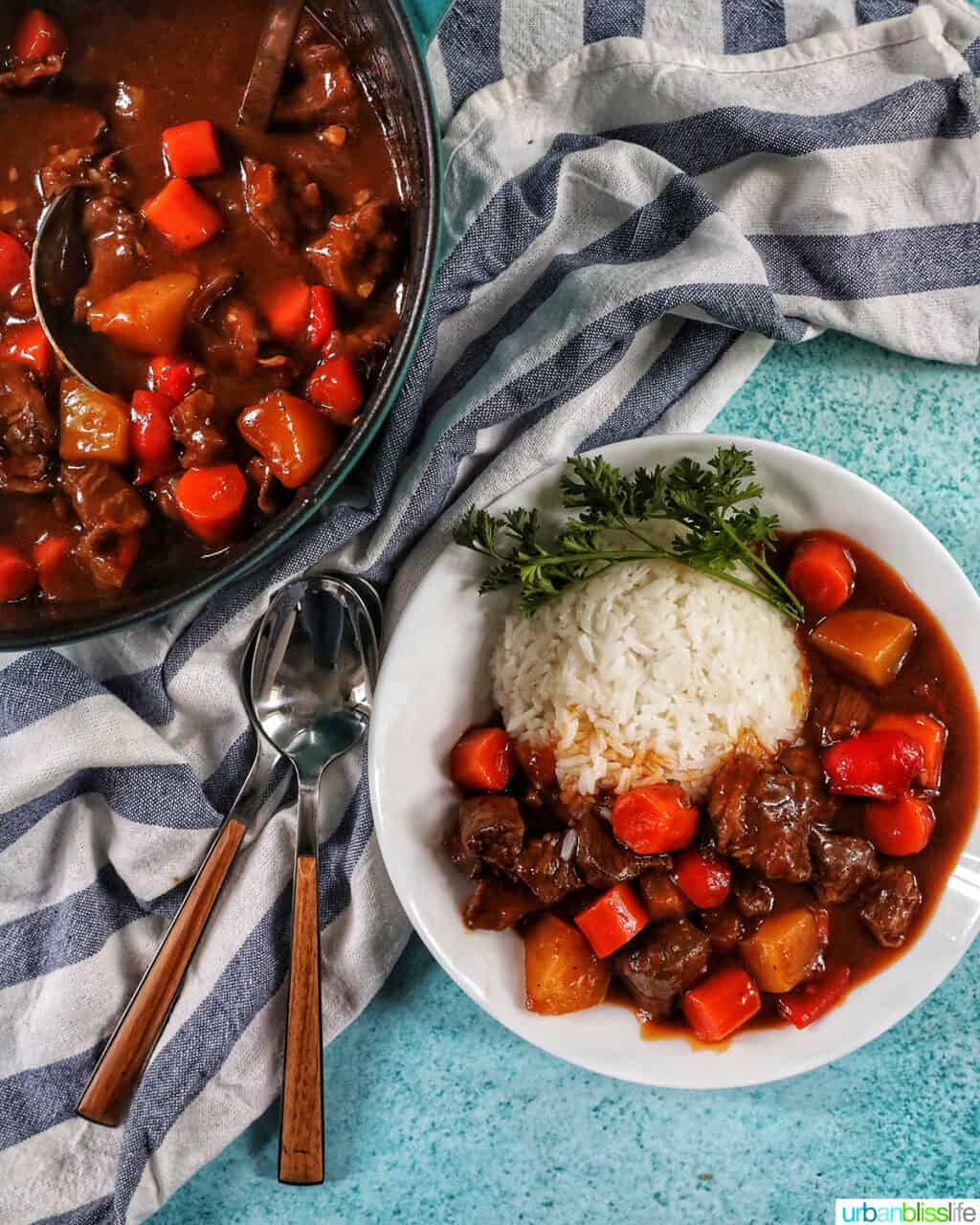 bowl of beef mechado next to a dutch oven of stew with striped napkin and utensils.