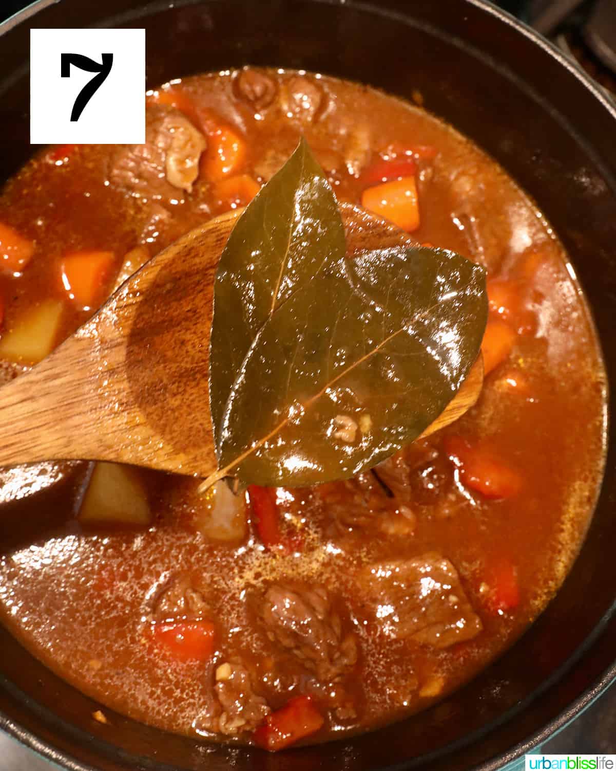 wooden spoon removing two bay leaves from cooked beef mechado.