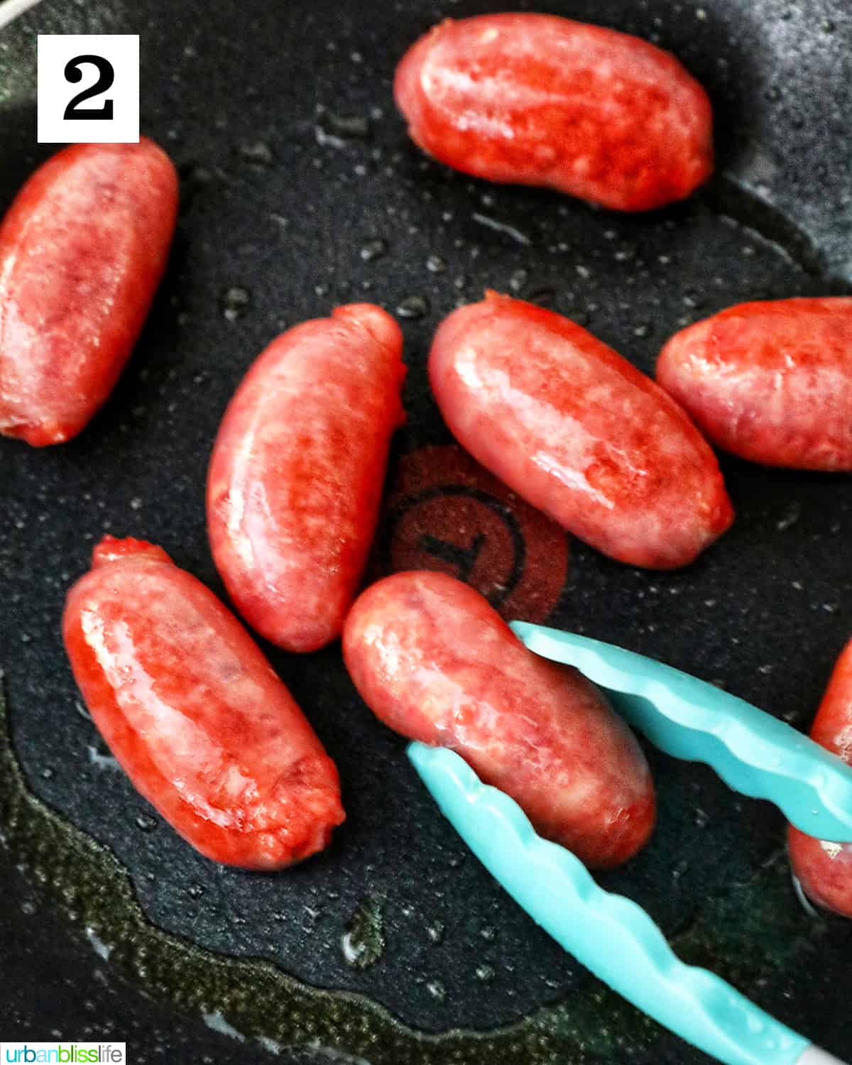 tongs holding longsilog (Filipino sausage) in a nonstick skillet.