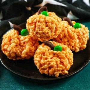 four pumpkin rice krispie treats on a black plate.