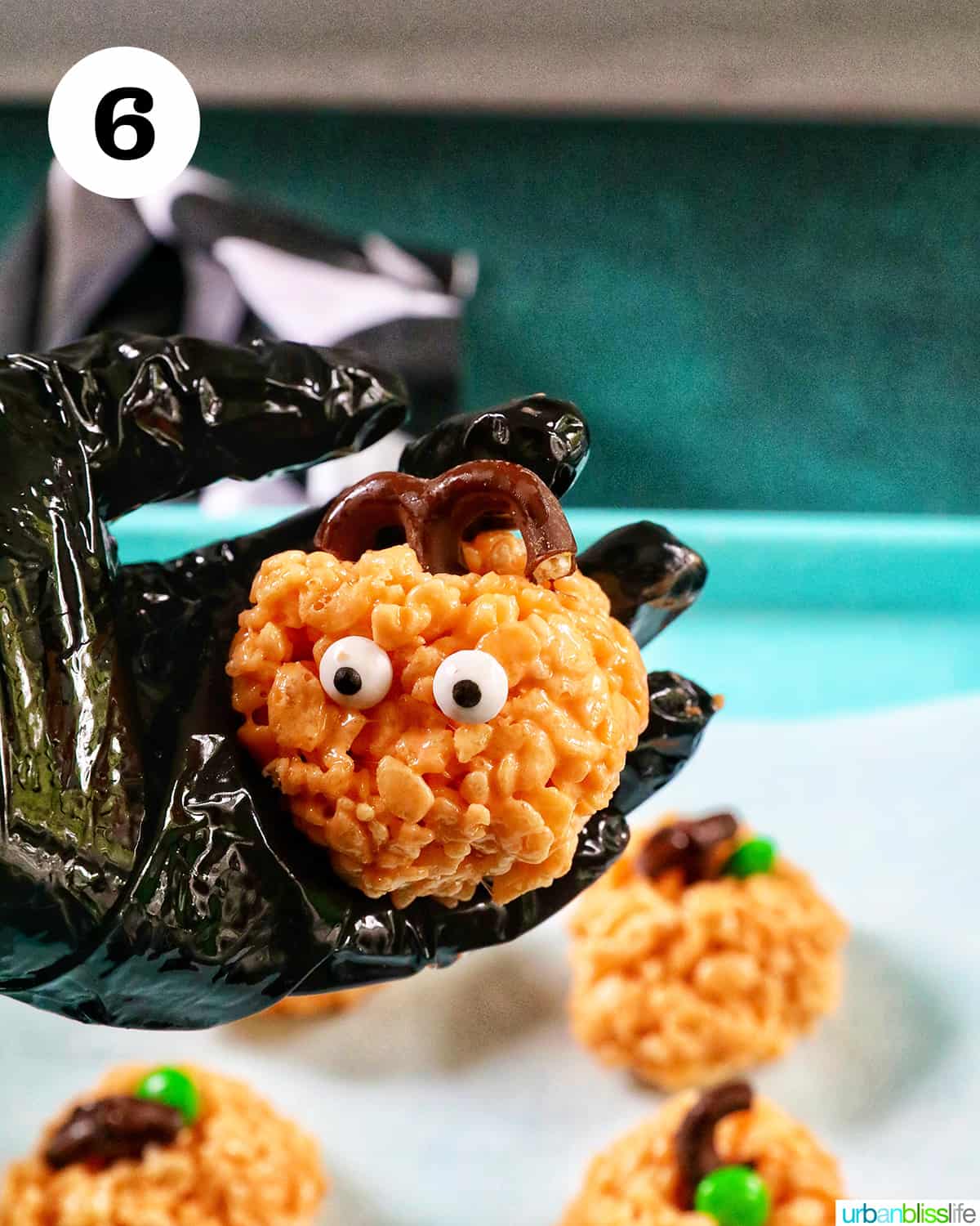 gloved hand holding a decorated pumpkin rice krispie treat