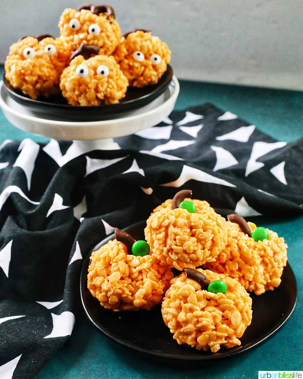 orange pumpkin rice krispie treats decorated two ways on black plates with black and white napkin.