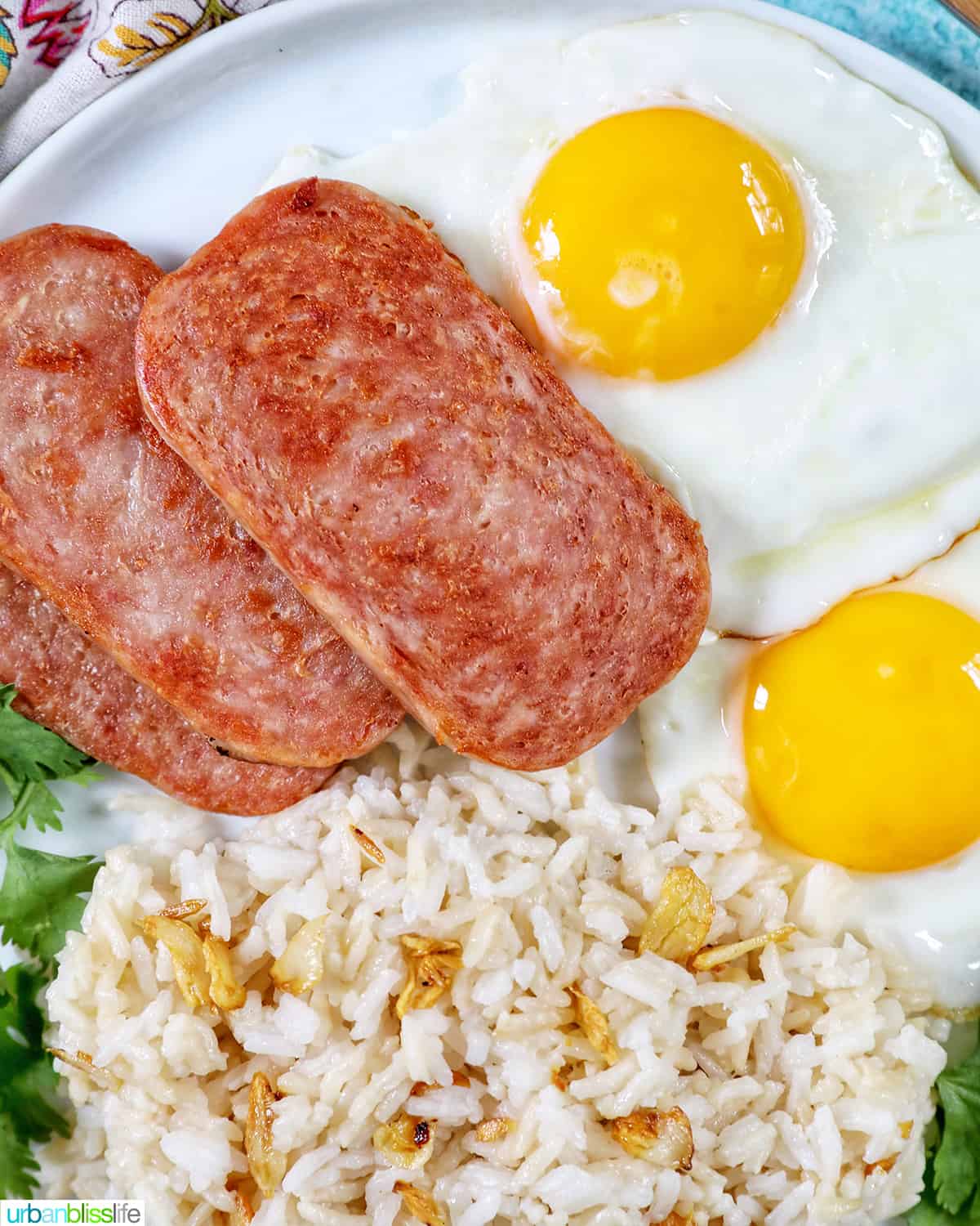 Plate of Spamsilog: slices of Spam, two eggs over easy, and Filipino Sinangag garlic rice with greens.