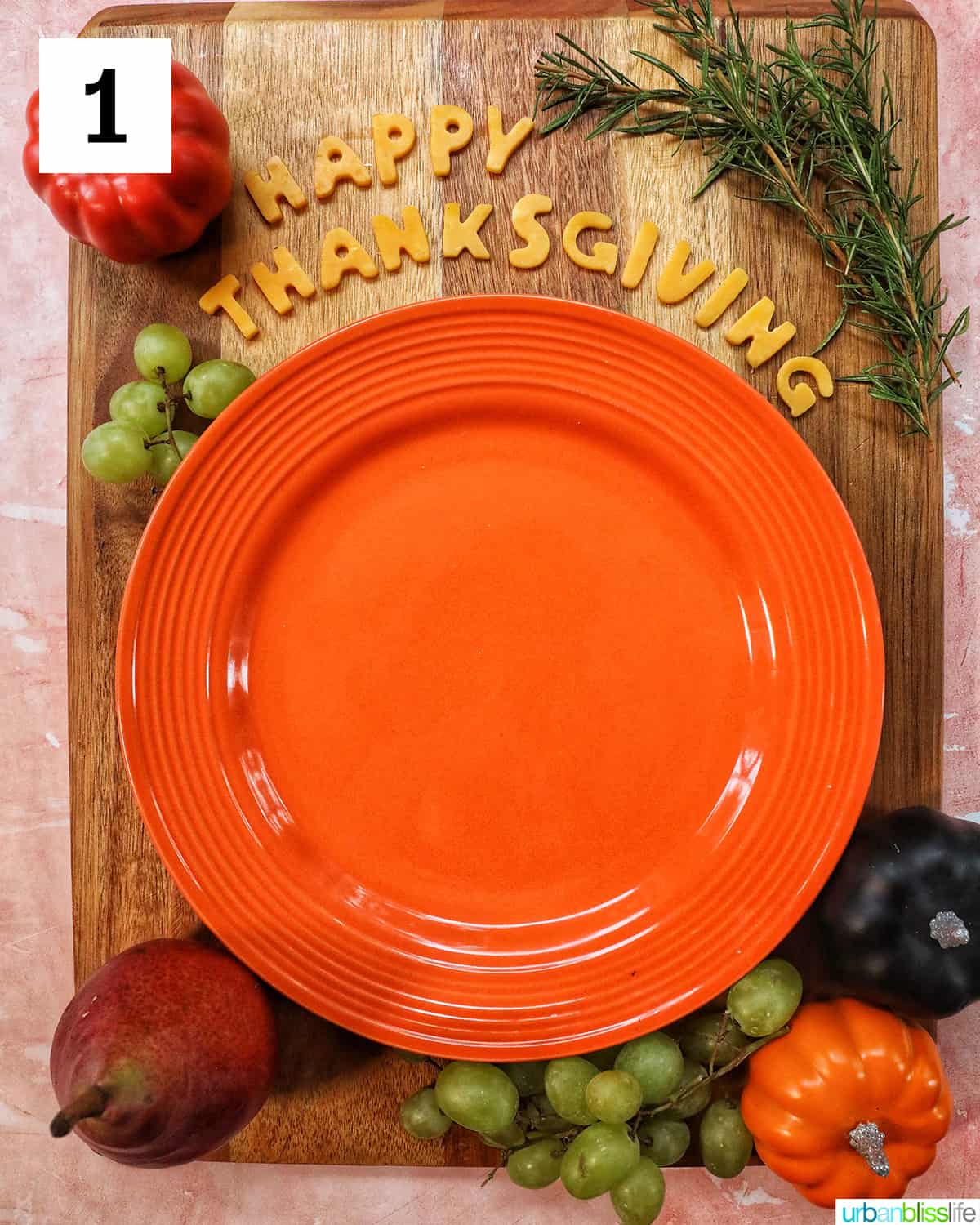 First layer of a Thanksgiving charcuterie board with Happy Thanksgiving cheese, orange plate, fruit on a wood board.