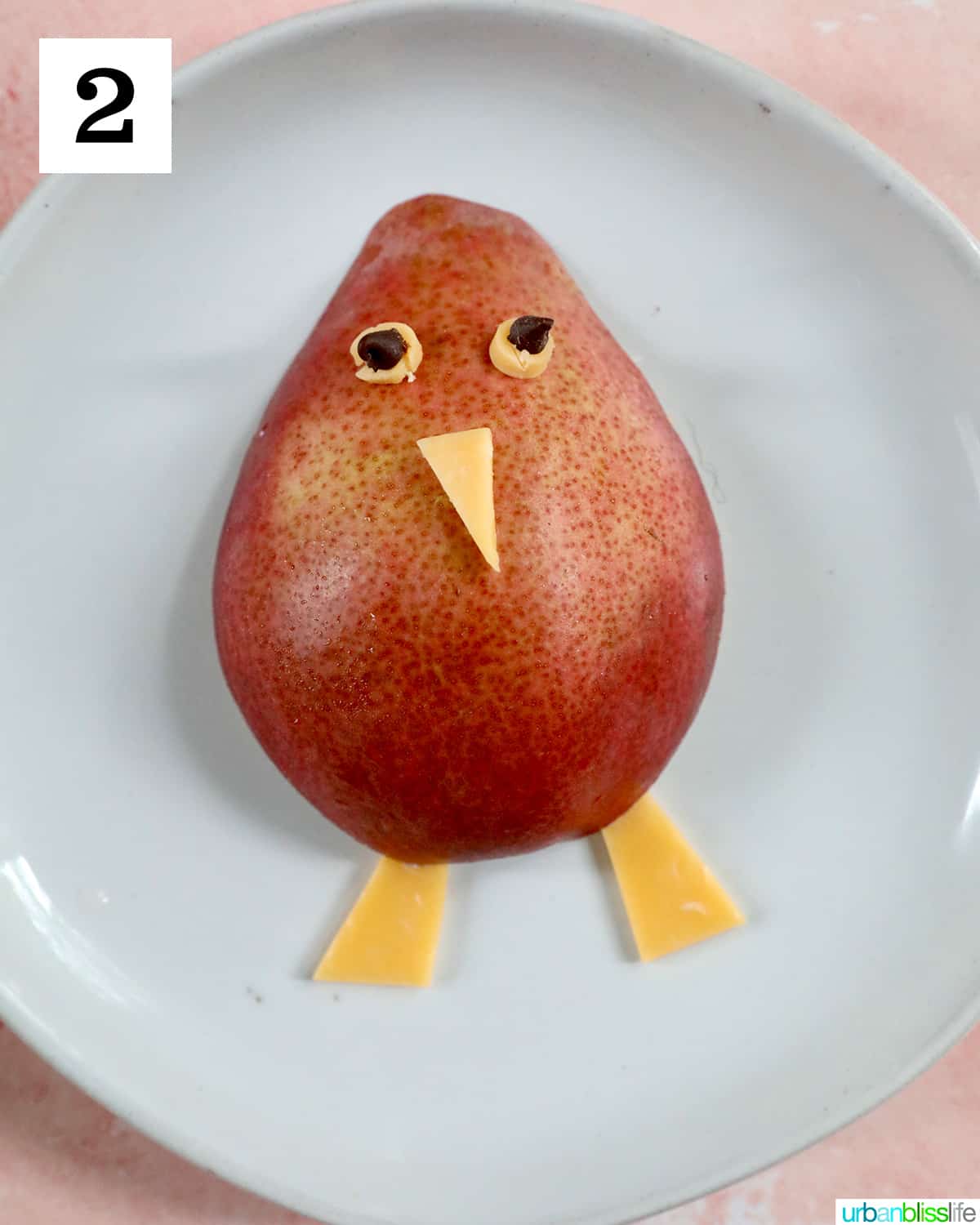 making a turkey out of a pear, cheese, on a white plate.