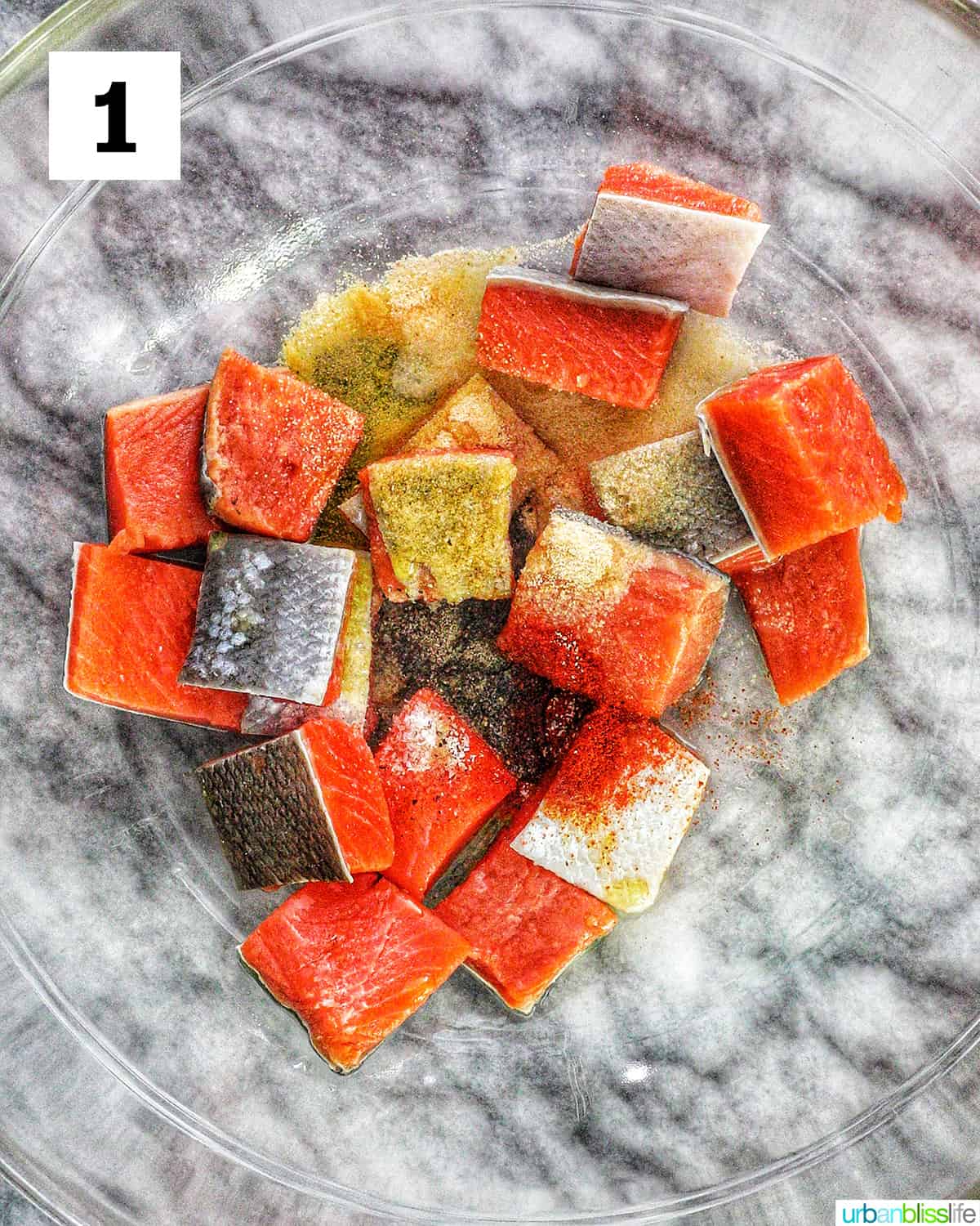 salmon pieces sprinkled with seasoning in a clear bowl.