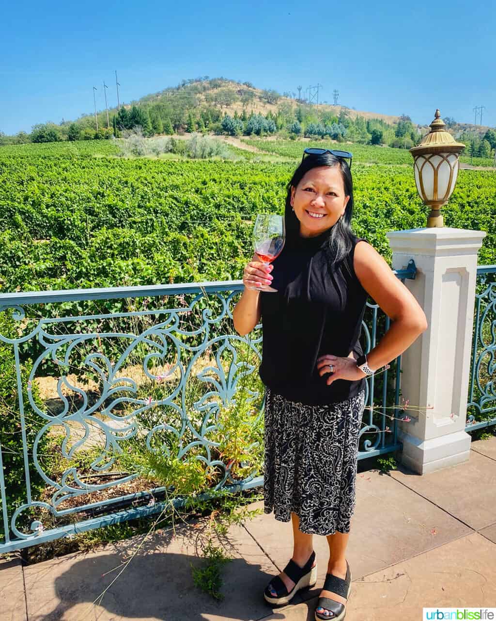Marlynn Schotland holding a glass of rosรฉ wine in front of Belle Fiore Winery vineyards