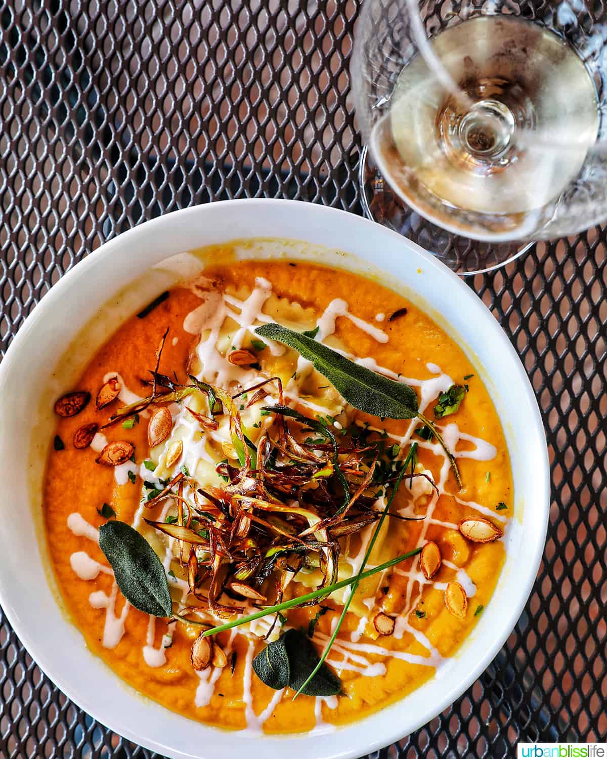 bowl of ravioli soup with glass of wine on a table.