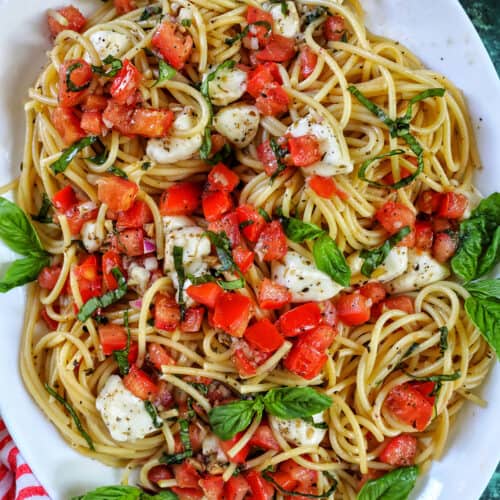 bruschetta pasta with tomatoes, basil, mozzarella cheese in a big white serving bowl.