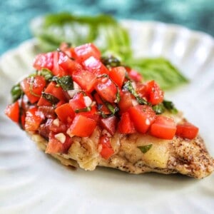 single bruschetta chicken on a white plate with basil leaves in the background.