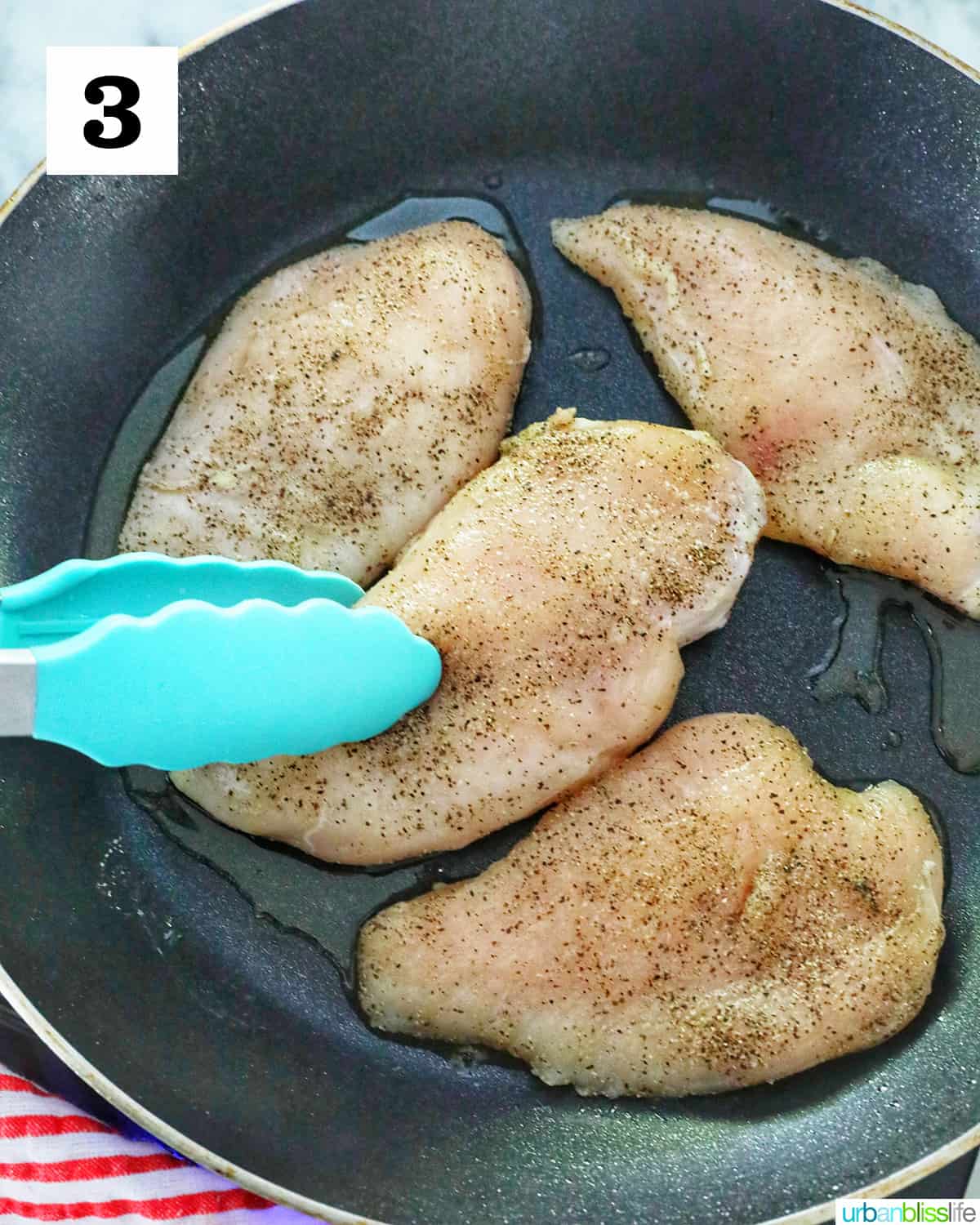 blue tongs turning over a chicken breast in a skillet with three other chicken breasts.