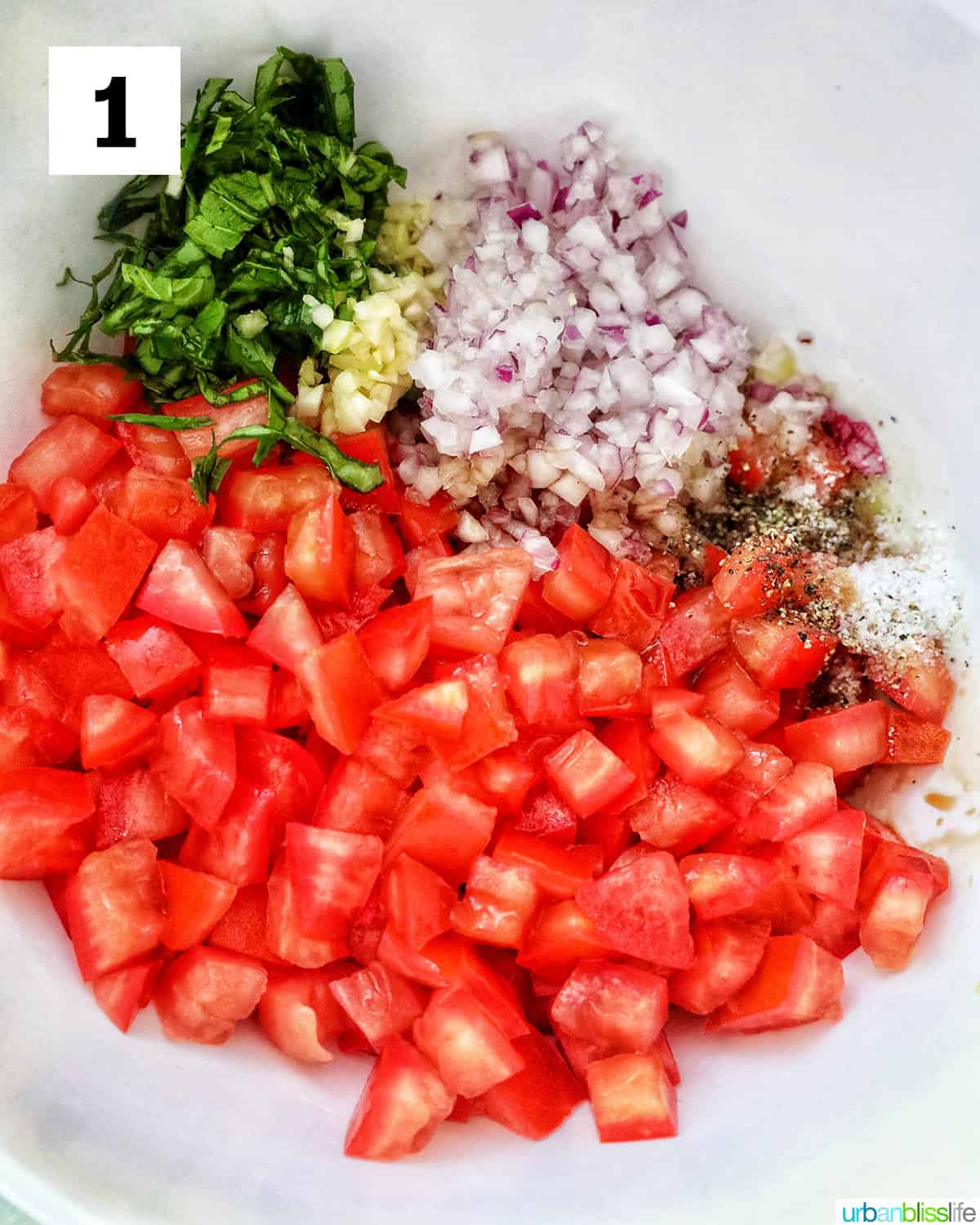 diced tomatoes, sliced basil, red onions and garlic in a white bowl to make bruschetta.
