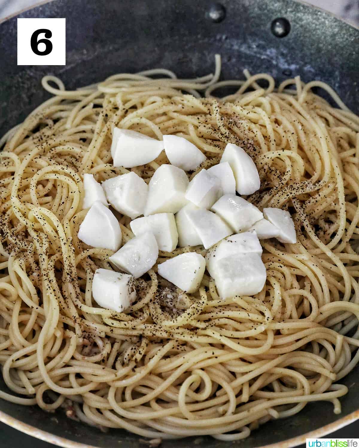 chopped mozzarella cheese on top of spaghetti in a skillet.