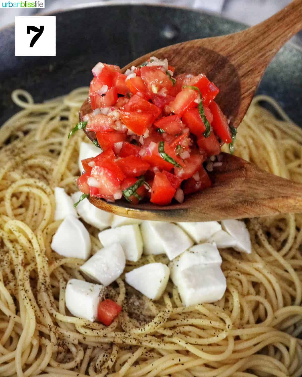 Adding chopped tomatoes and mozzarella to spaghetti.