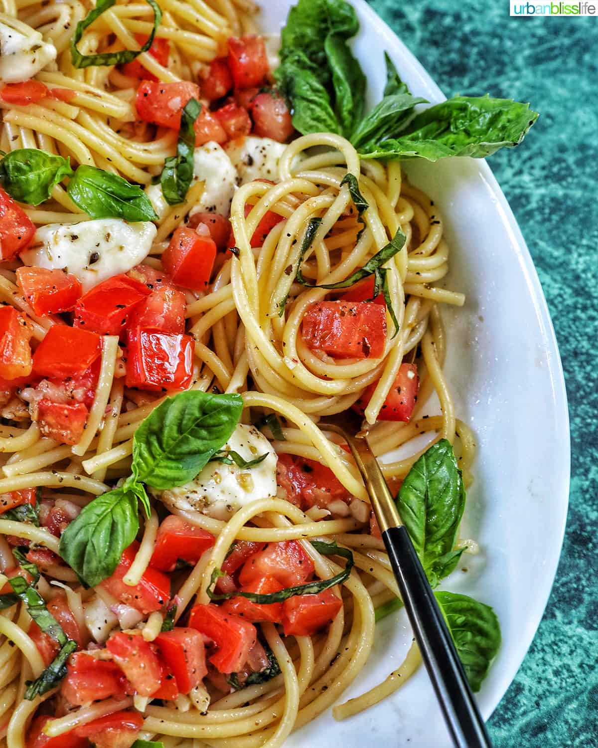 bruschetta pasta with tomatoes, basil, mozzarella cheese in a big white serving bowl.