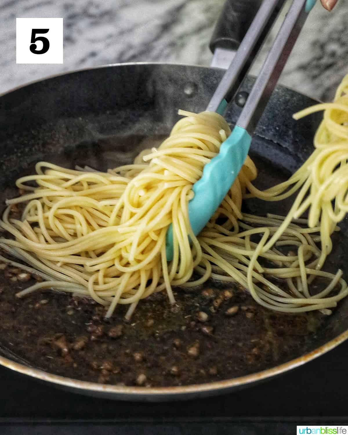 tongs tossing spaghetti pasta in a skillet.