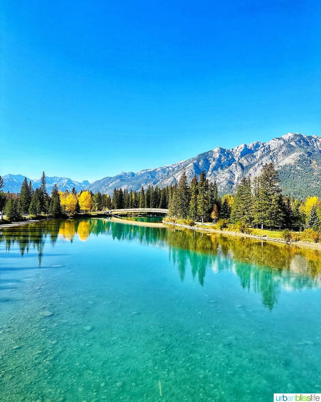 beautiful turquoise blue Bow River, footbridge, and mountains in Banff Canada.