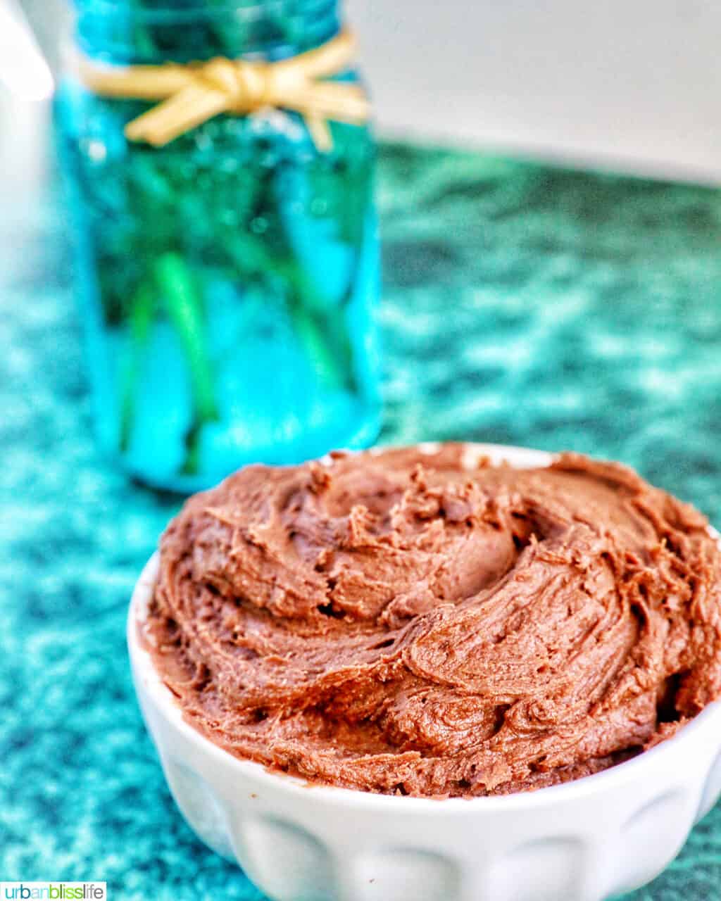chocolate buttercream frosting in a white bowl on green marble table.