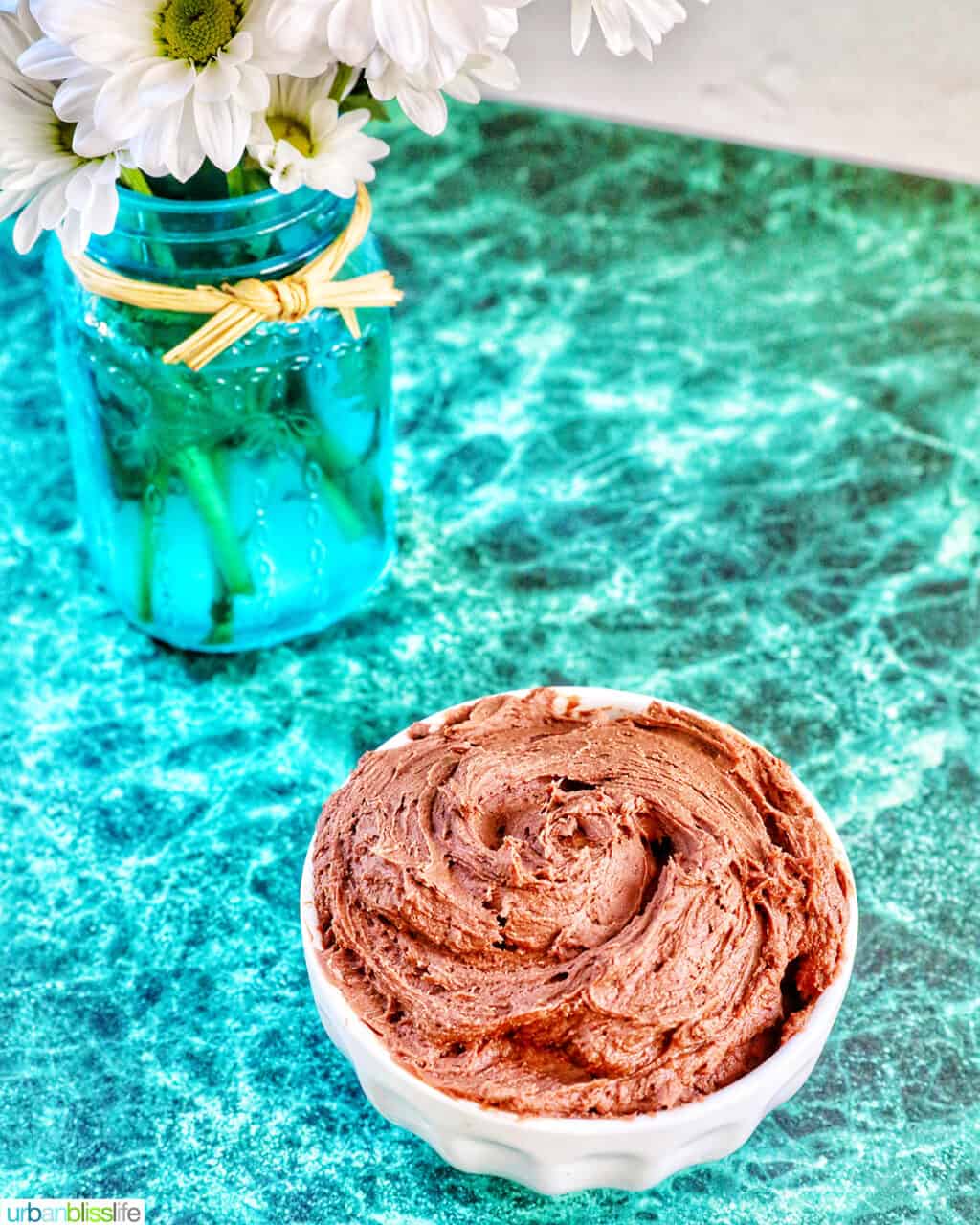 chocolate buttercream frosting in a white bowl on a green marble table.