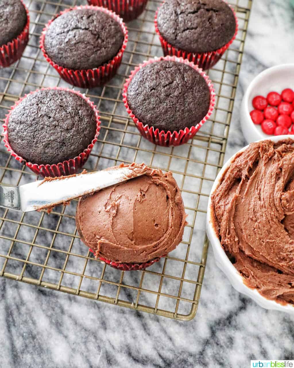 frosting a chocolate cupcake with chocolate buttercream with cupcakes in the background.