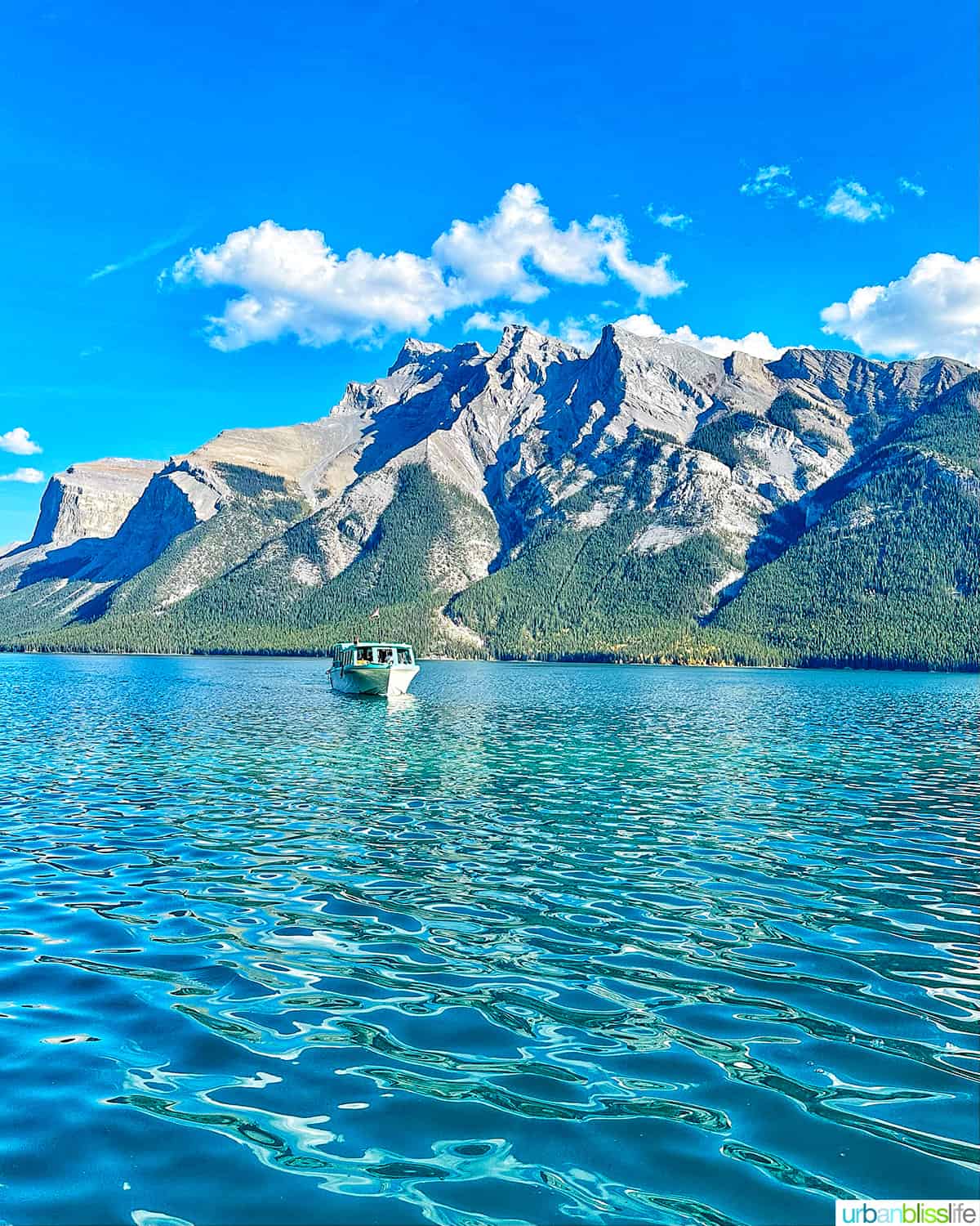 boat cruising on Lake Minnewanka with mountains in the background.