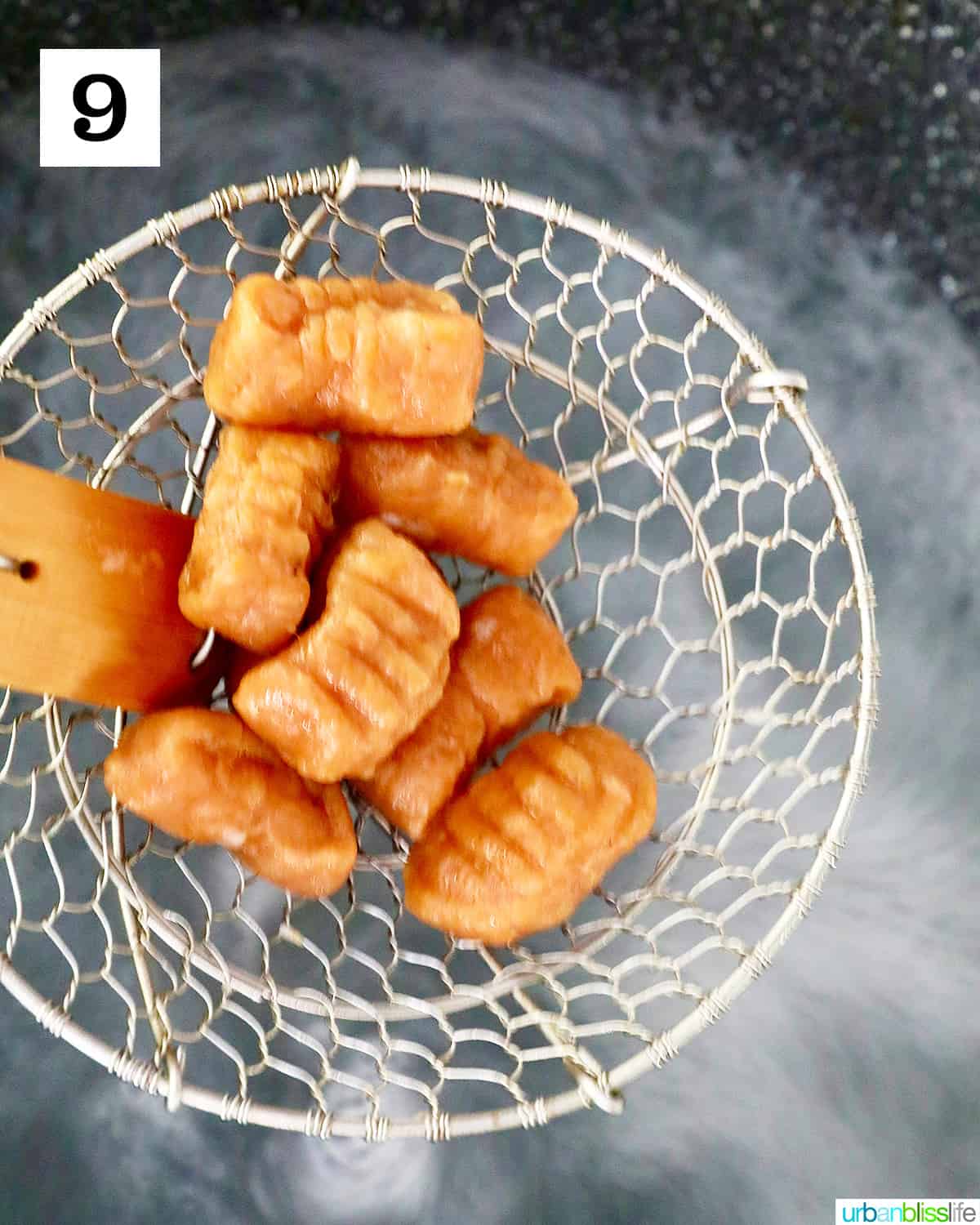 kitchen wire spider holding cooked shaped pumpkin gnocchi over boiling water.