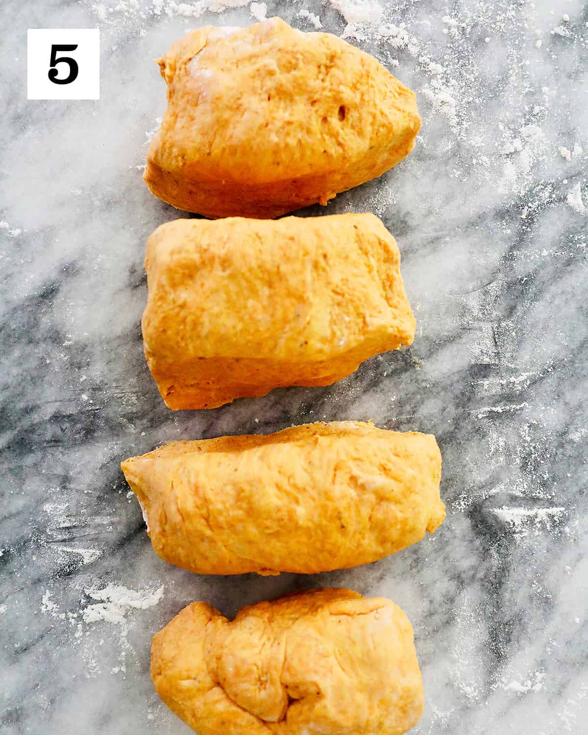 pumpkin gnocchi dough divided into four equal portions on a marble countertop.