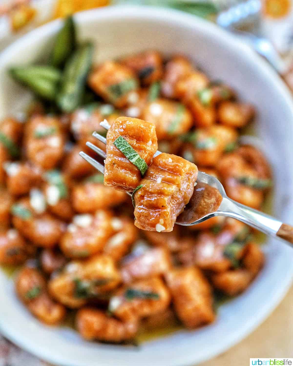fork holding two pieces of pumpkin gnocchi closeup over a bowl of pumpkin gnocchi.
