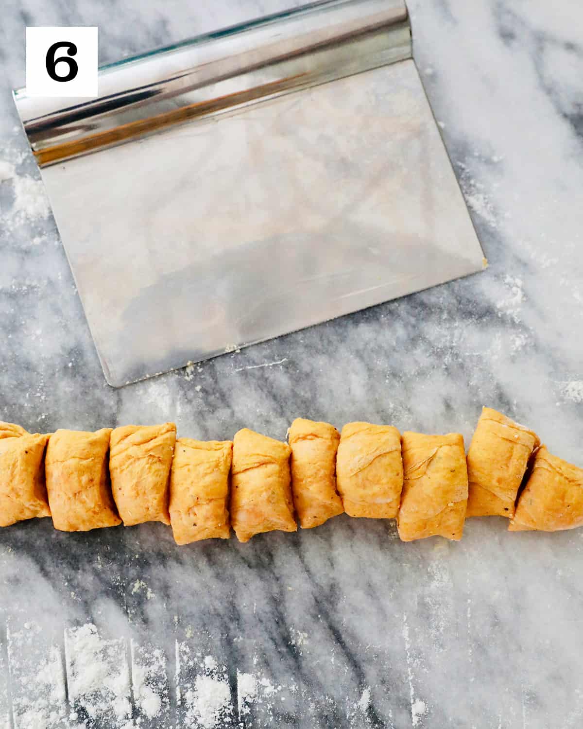 pastry cutter slicing pumpkin gnocchi dough into small equal portions on a marble countertop.