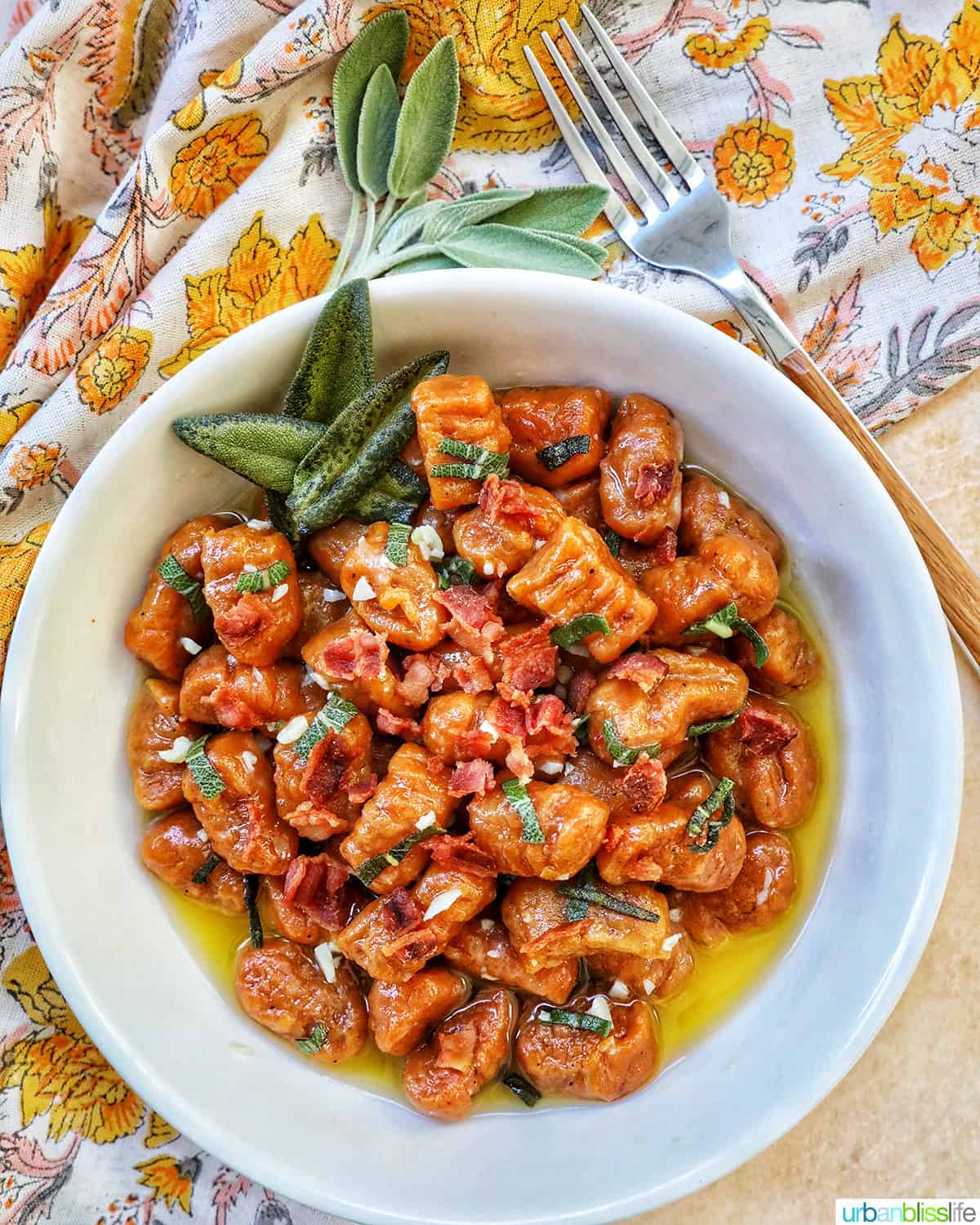 bowl of pumpkin gnocchi with sage and bacon, with a fork and colorful napkin above it.