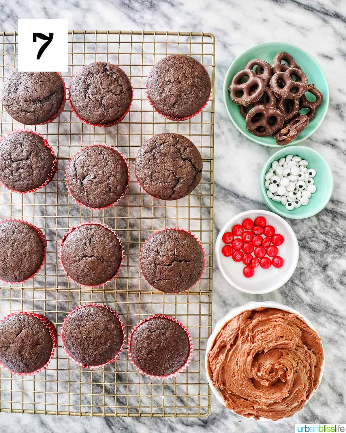 rows of chocolate cupcakes on a wire rack with chocolate buttercream and decorations on the side.