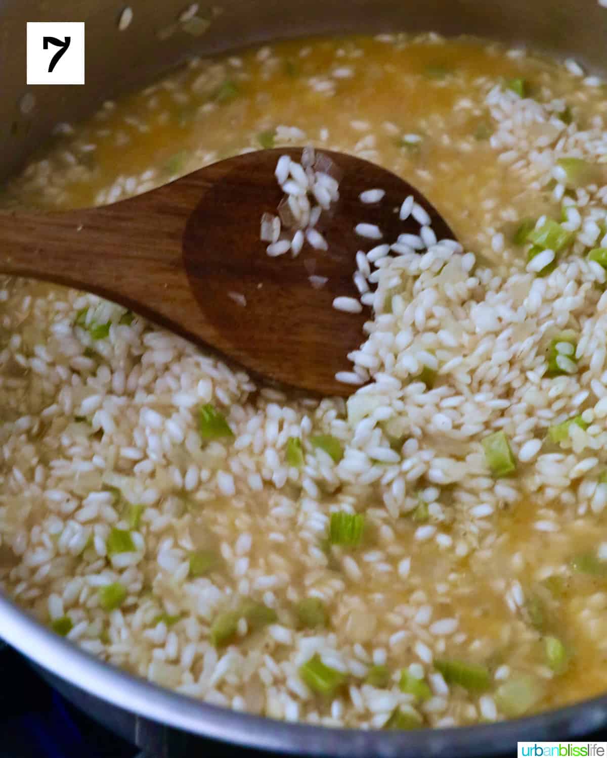 prawn stock added to the rice and vegetables with a wooden spoon mixing them all together.