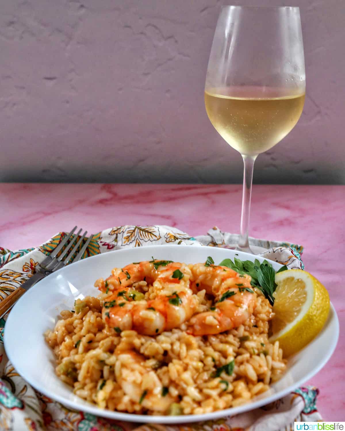 risotto with prawns in a white bowl with a glass of white wine behind it.