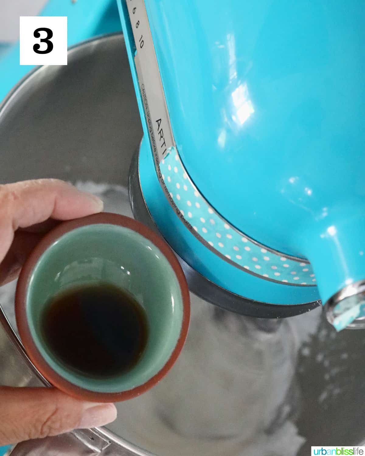 hand holding a bowl of vanilla extract adding to stand mixer to make royal icing.