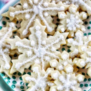 plate full of snowflake sugar cookies decorated with royal icing and decorator sugar.