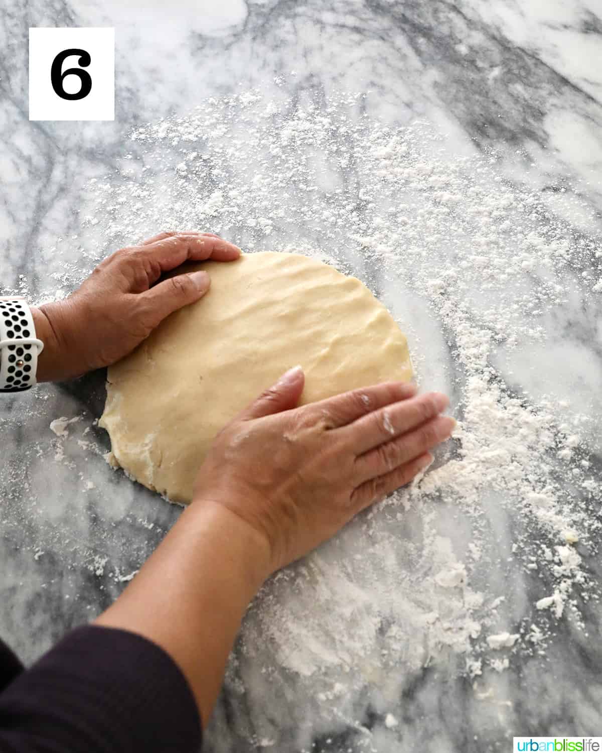 hands forming cookie dough into a disc on marble countertop.