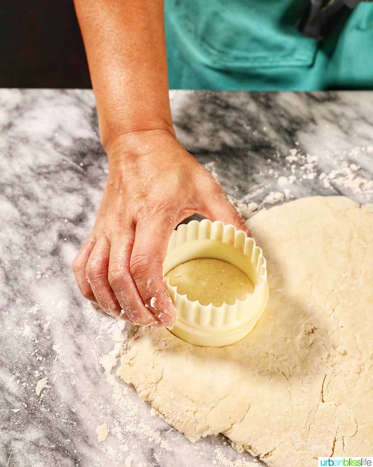 hand holding a biscuit cutter over biscuit dough on a marble counter.