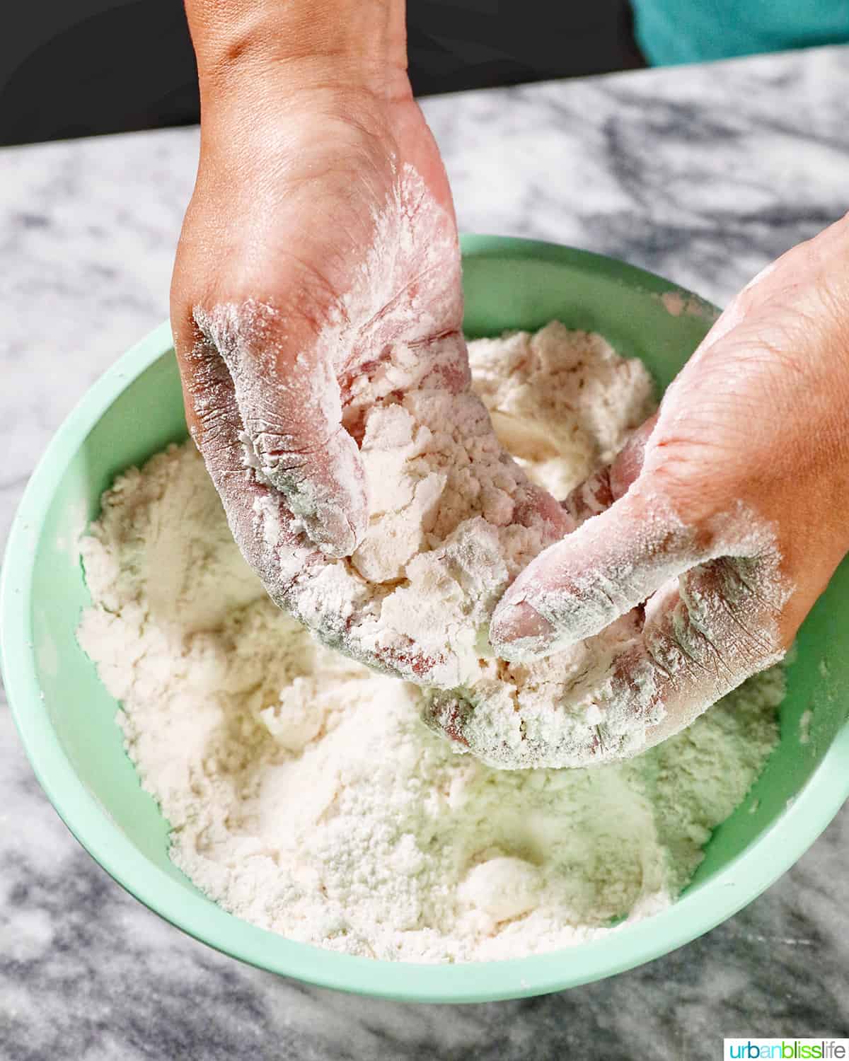 hands cutting cold butter into biscuit dough.