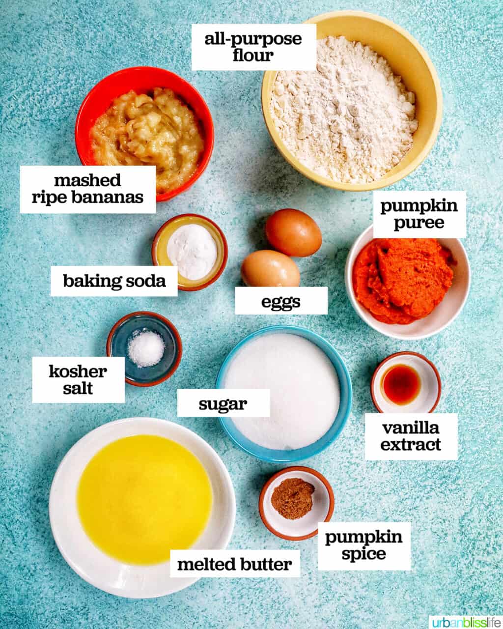 bowls filled with ingredients to make pumpkin banana muffins on top of a bright blue table.