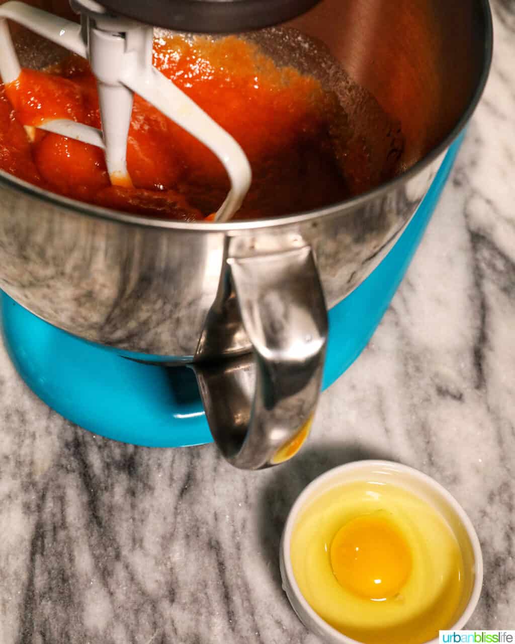 bowl with egg ready to be mixed into the orange pumpkin banana muffin batter in the blue stand mixer.