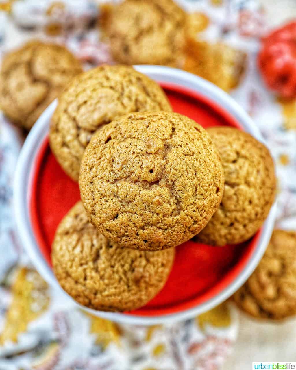 pumpkin banana muffins stacked on an orange plate on top of a floral napkin.