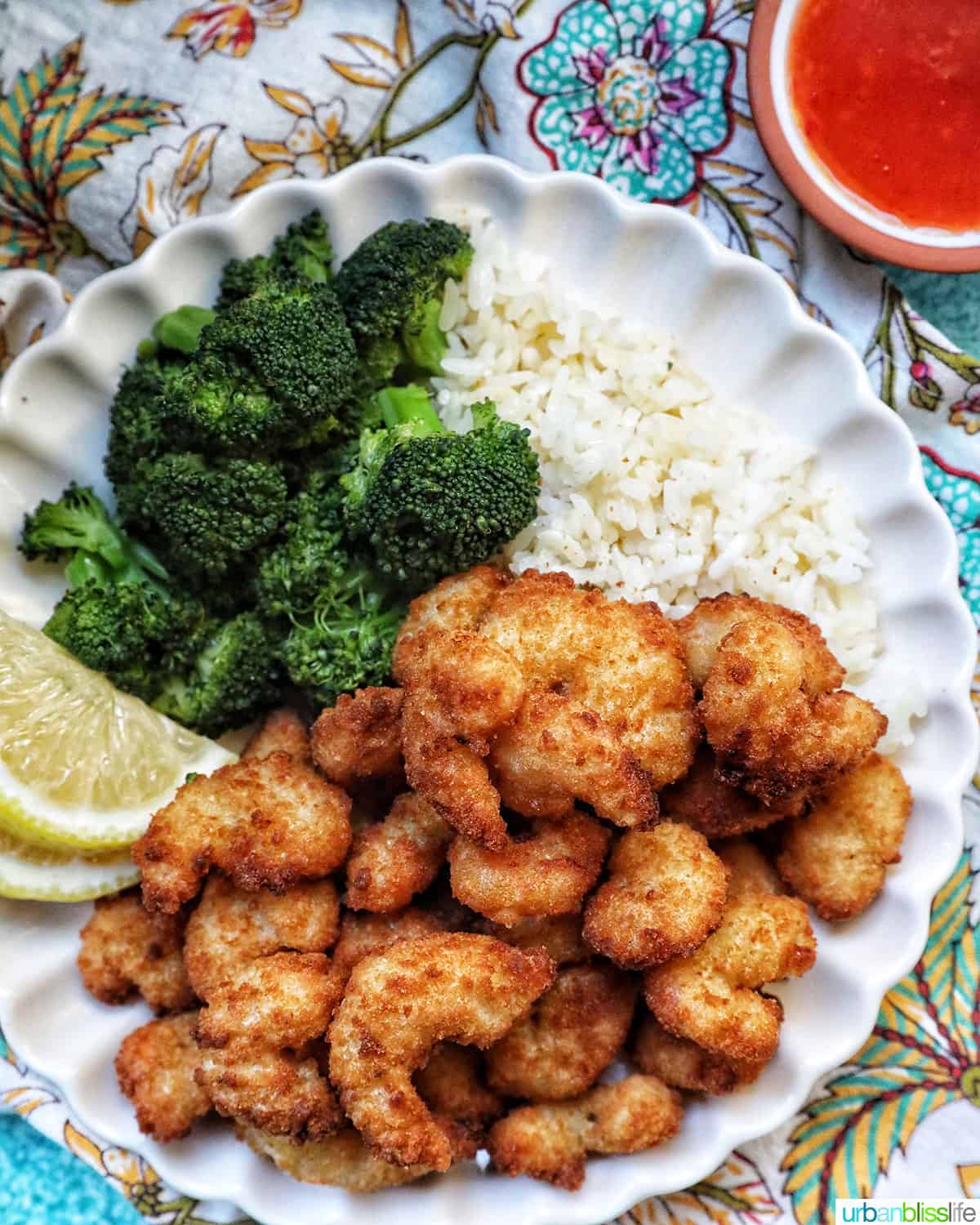 airfryer popcorn shrimp on a plate with broccoli, lemon wedges, and side of cocktail sauce.
