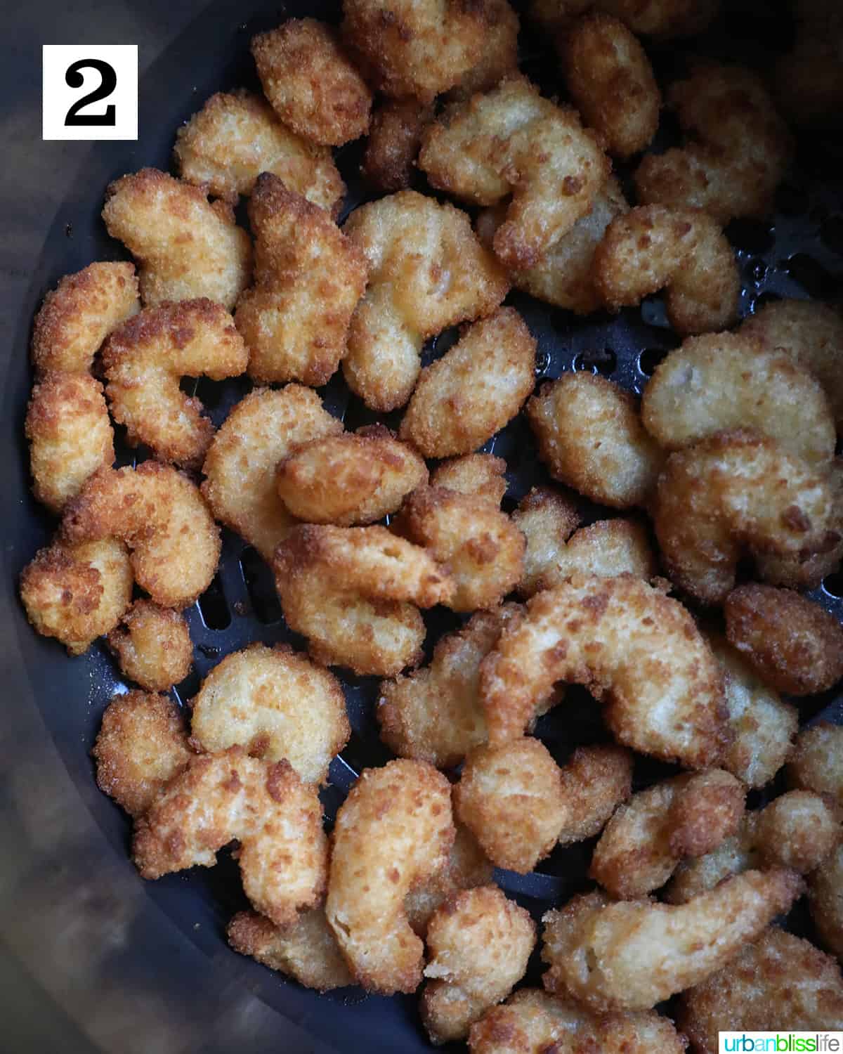 adding frozen popcorn shrimp to the air fryer basket.