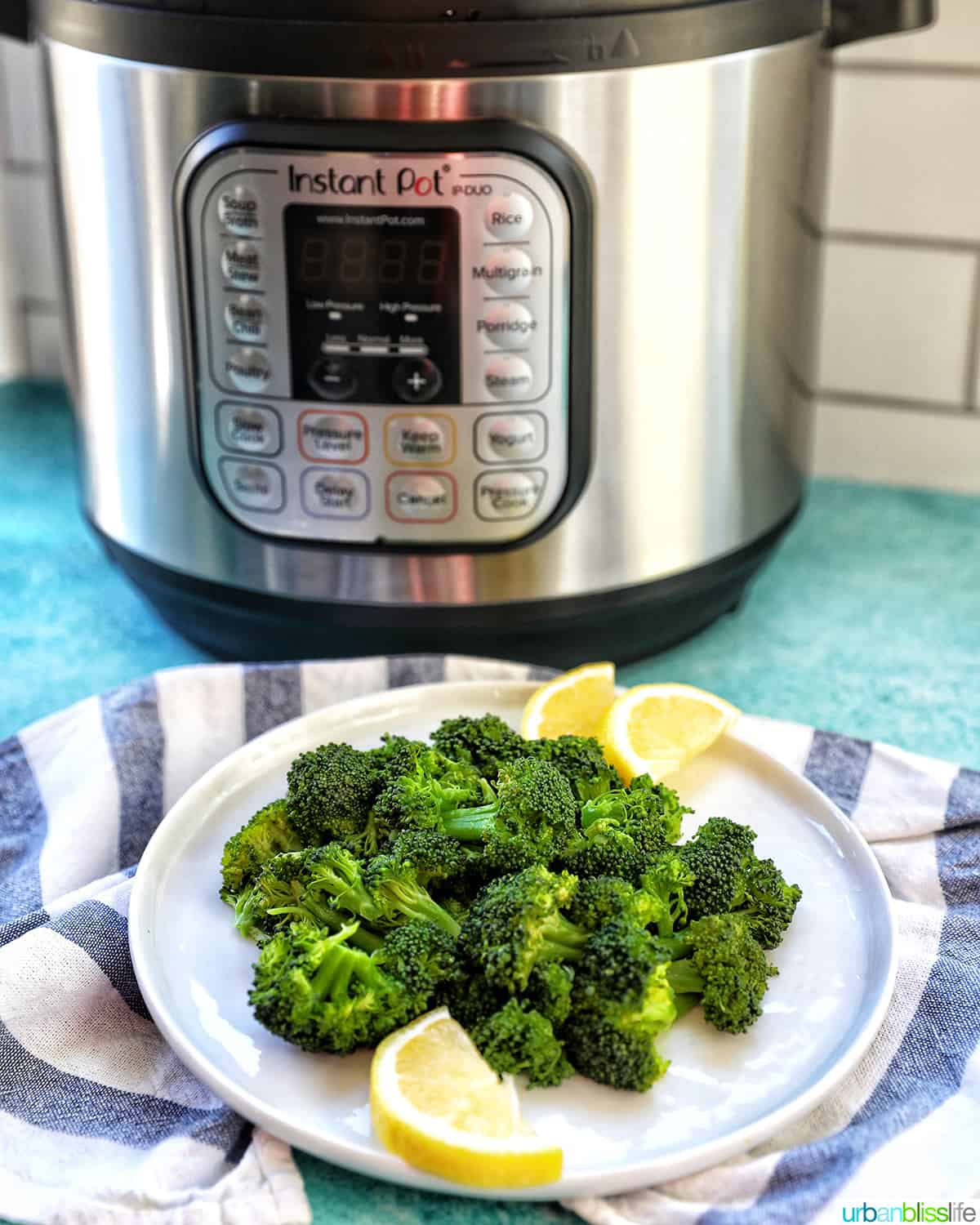 pressure cooked broccoli in a plate with lemon wedges with an Instant Pot pressure cooker behind.