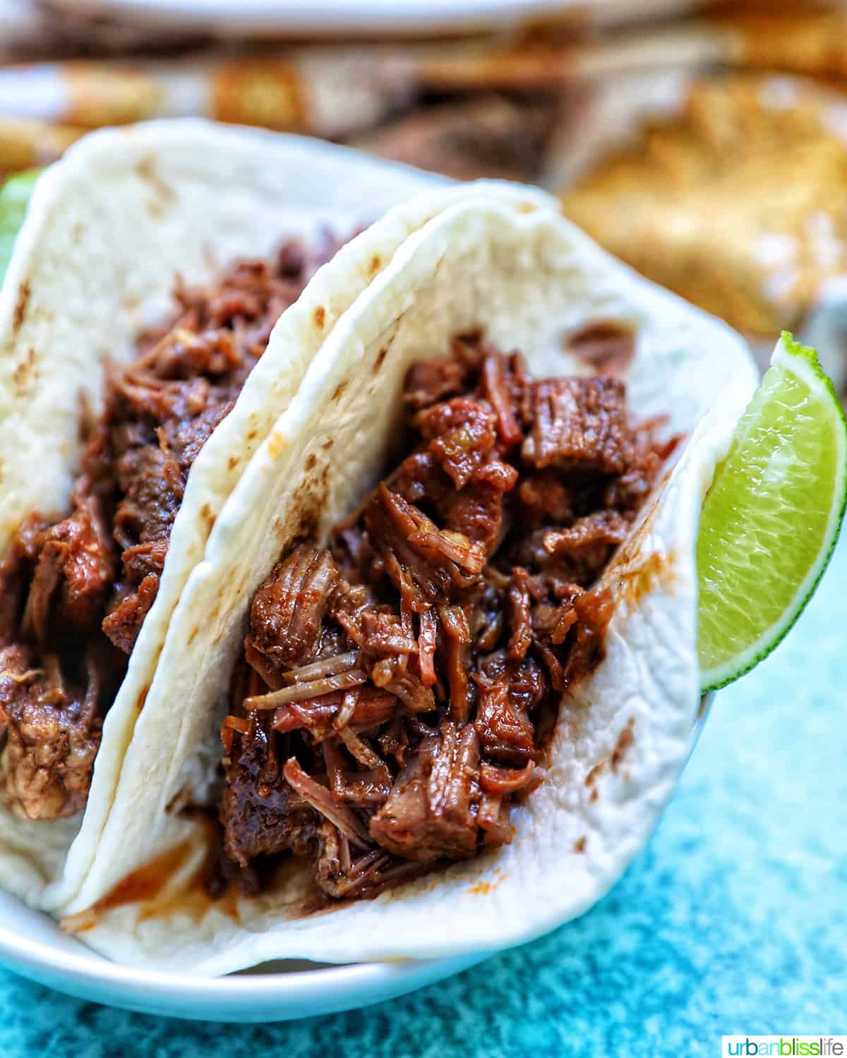 Mexican shredded beef in taco shells with lime wedges.