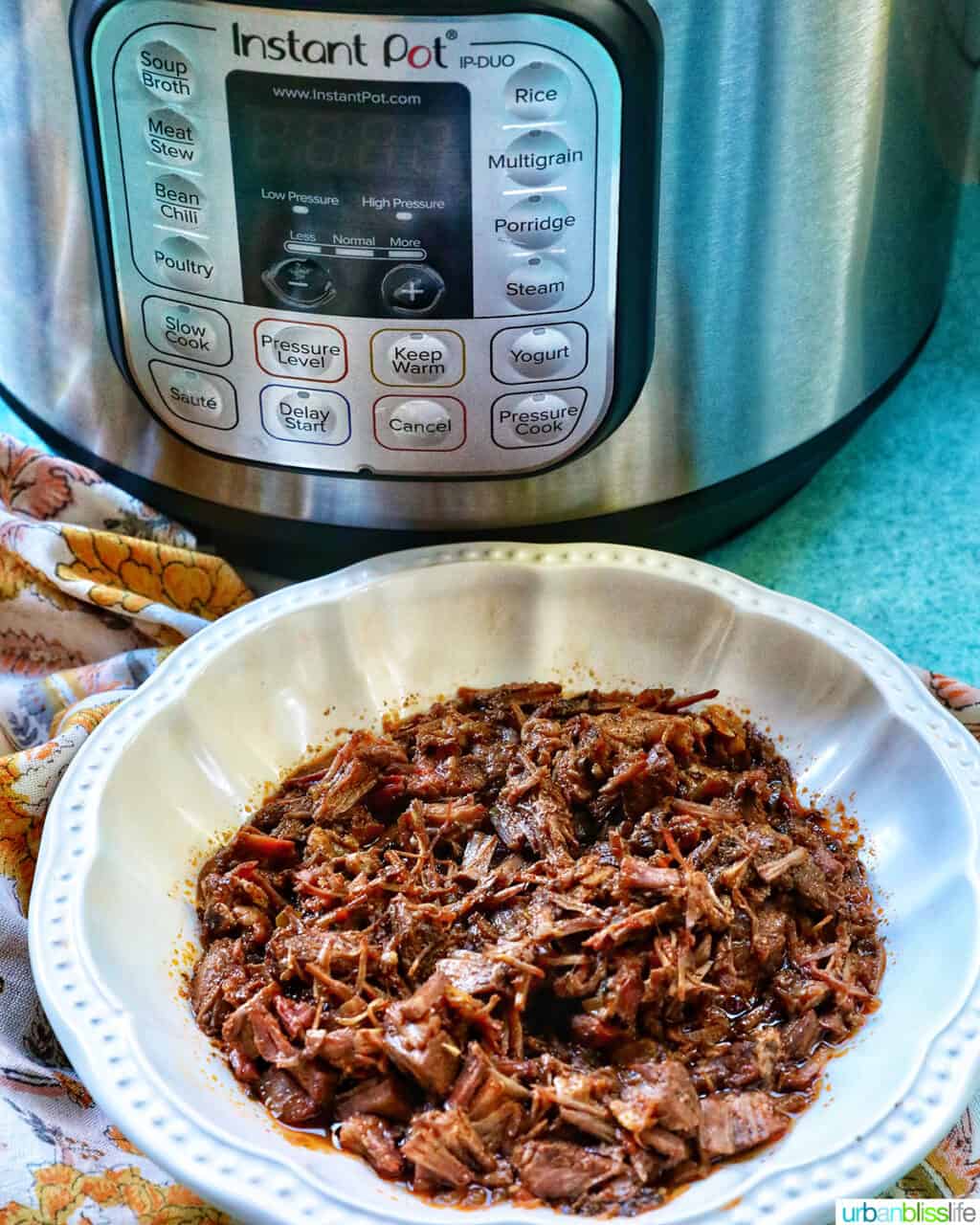 bowl of Mexican shredded beef in front of an Instant Pot pressure cooker.
