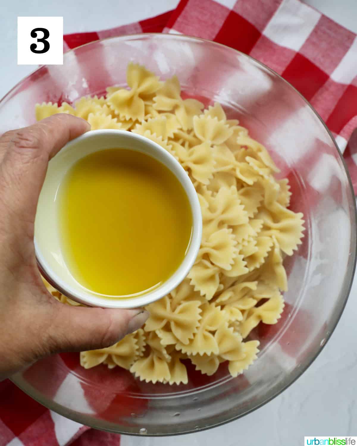 hand holding olive oil over pasta.